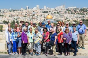 A large group of people smile for the photo in front of the Jerusalem city background 